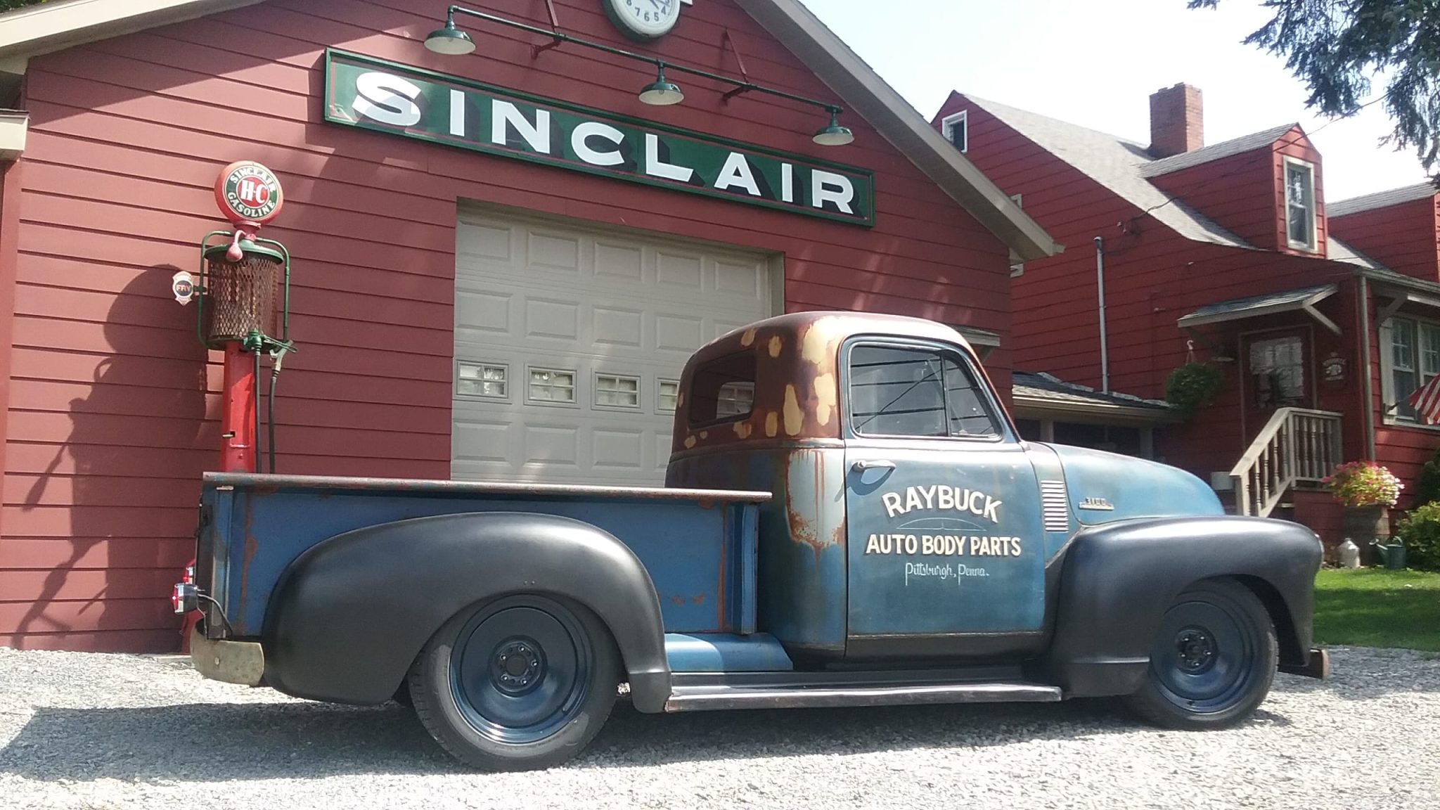 A classic 1953 Chevy Truck with RAYBUCK AUTO BODY PARTS painted on it next to a garage
